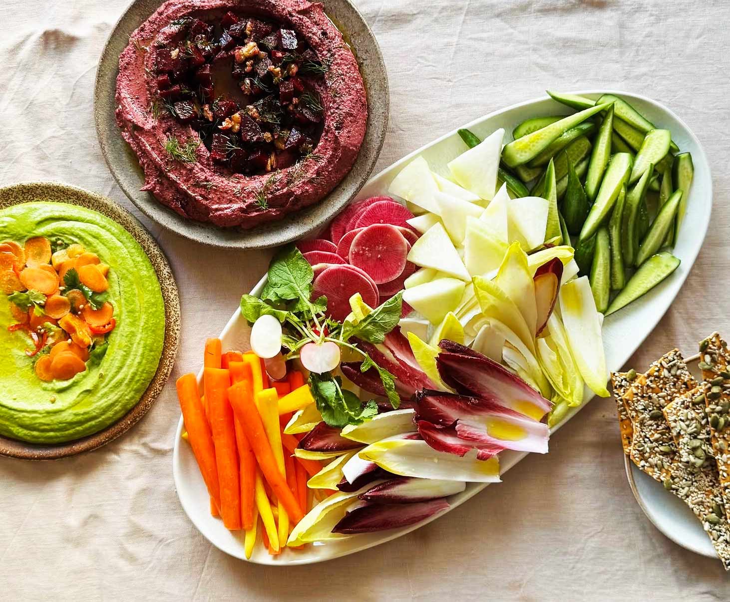 A spread of crudités with beet, herb, and carrot-topped hummus dips